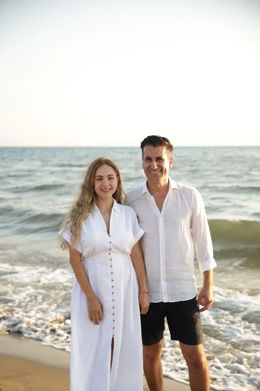 Fatma and Oğuzhan standing together at the water's edge in the late afternoon light.
