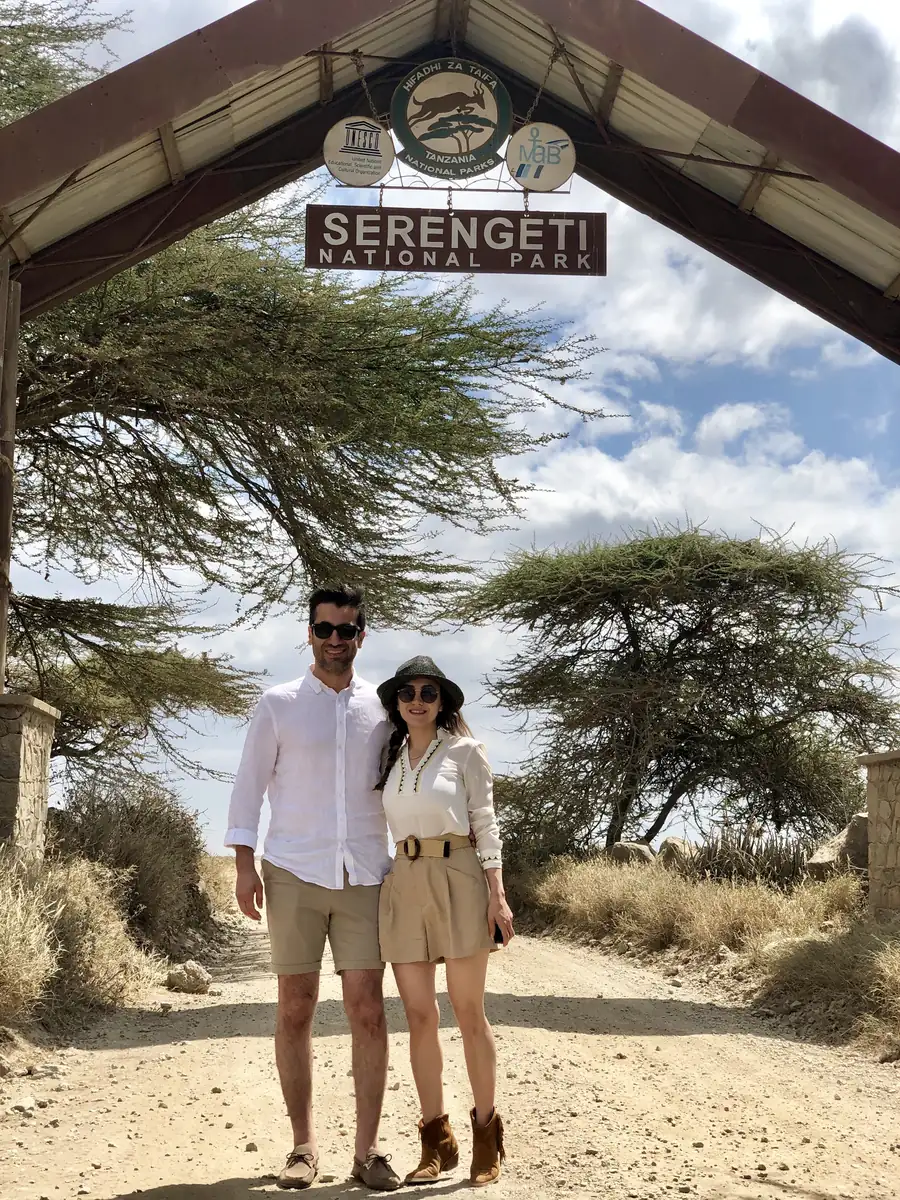 Fatma and Oğuzhan standing together on the dirt road under the Serengeti National Park entrance sign.
